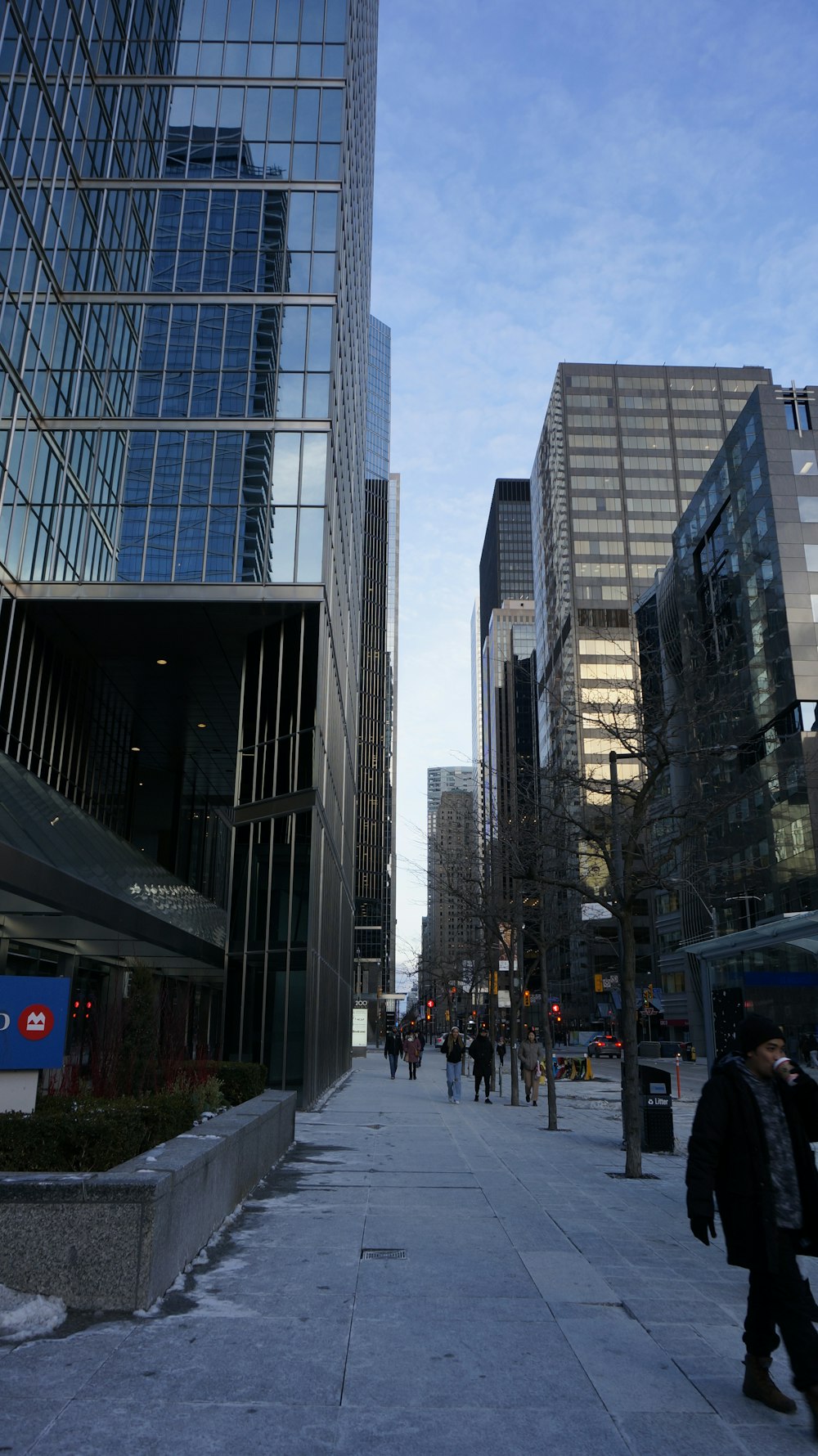a group of people walking down a sidewalk next to tall buildings