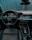 A modern car interior featuring a sleek, black dashboard with digital displays and controls. There's a prominent steering wheel with an Audi logo, and the seats are upholstered in black leather with red stitching. The overall design is high-tech and ergonomic.
