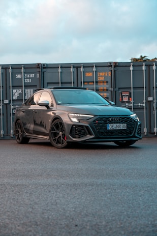 a grey car parked in front of a shipping container