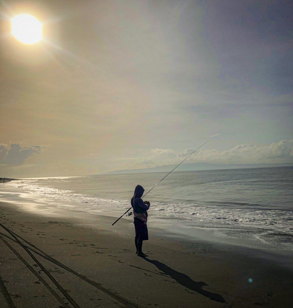 a person standing on a beach holding a fishing pole