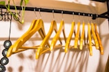 A row of wooden hangers neatly arranged on a black metal clothing rod. The hangers are evenly spaced and create a symmetrical pattern. A small green plant with dangling vines is attached to the left side of the rod, and a beaded accessory with circular patterns hangs beside it.