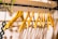 A row of wooden hangers neatly arranged on a black metal clothing rod. The hangers are evenly spaced and create a symmetrical pattern. A small green plant with dangling vines is attached to the left side of the rod, and a beaded accessory with circular patterns hangs beside it.