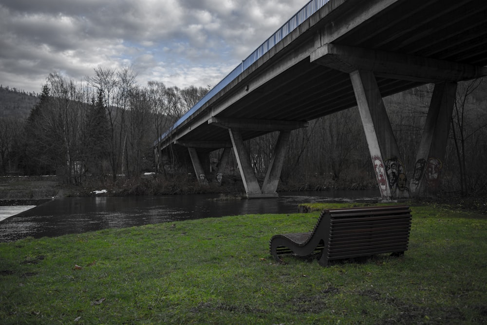 a bench sitting in the grass near a bridge