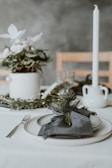 A minimalist dining table set with elegant tableware and a centerpiece of seasonal greenery.