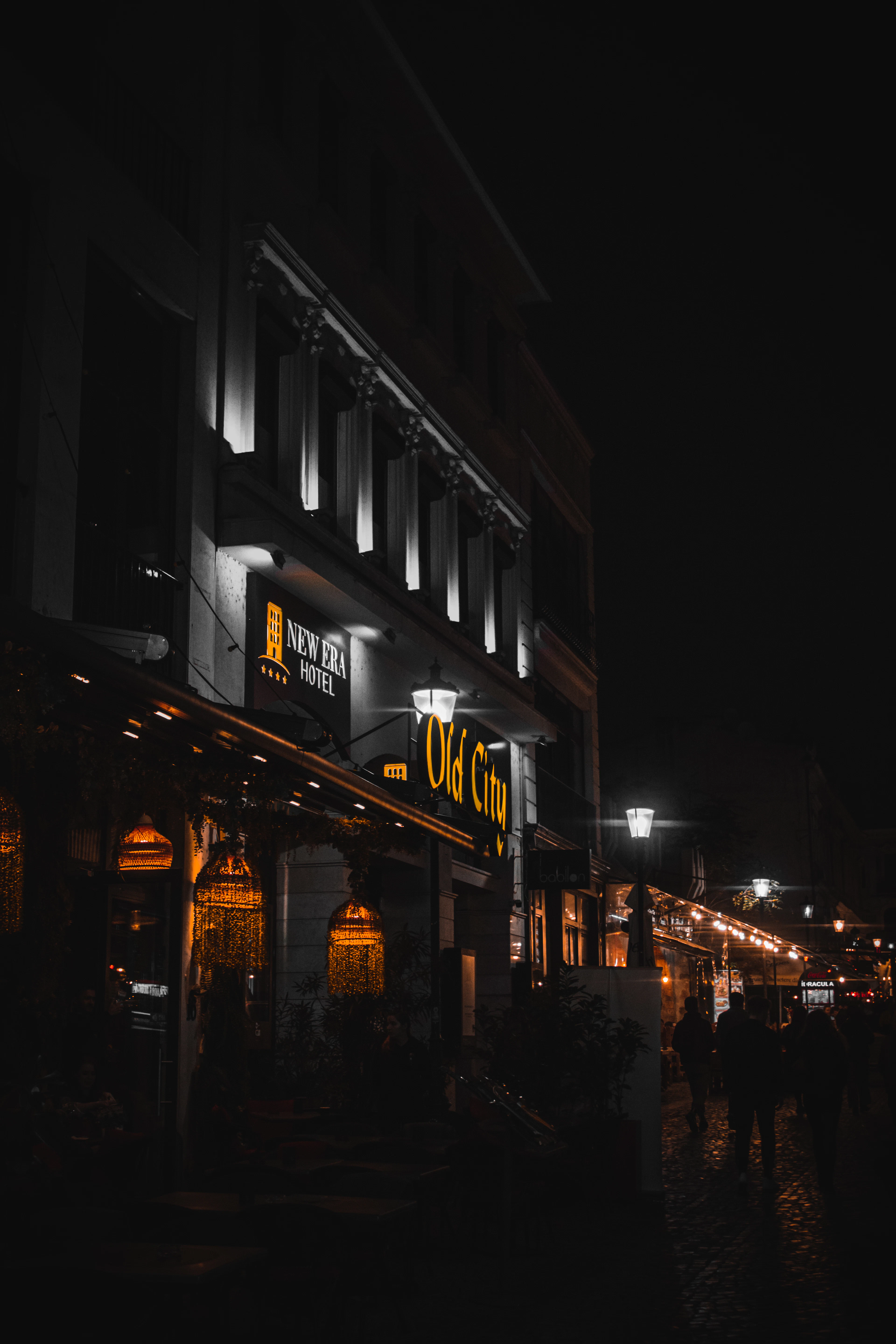 Illuminated Old City signage and string lights glow above a cobblestone street at night, silhouetting passersby.
