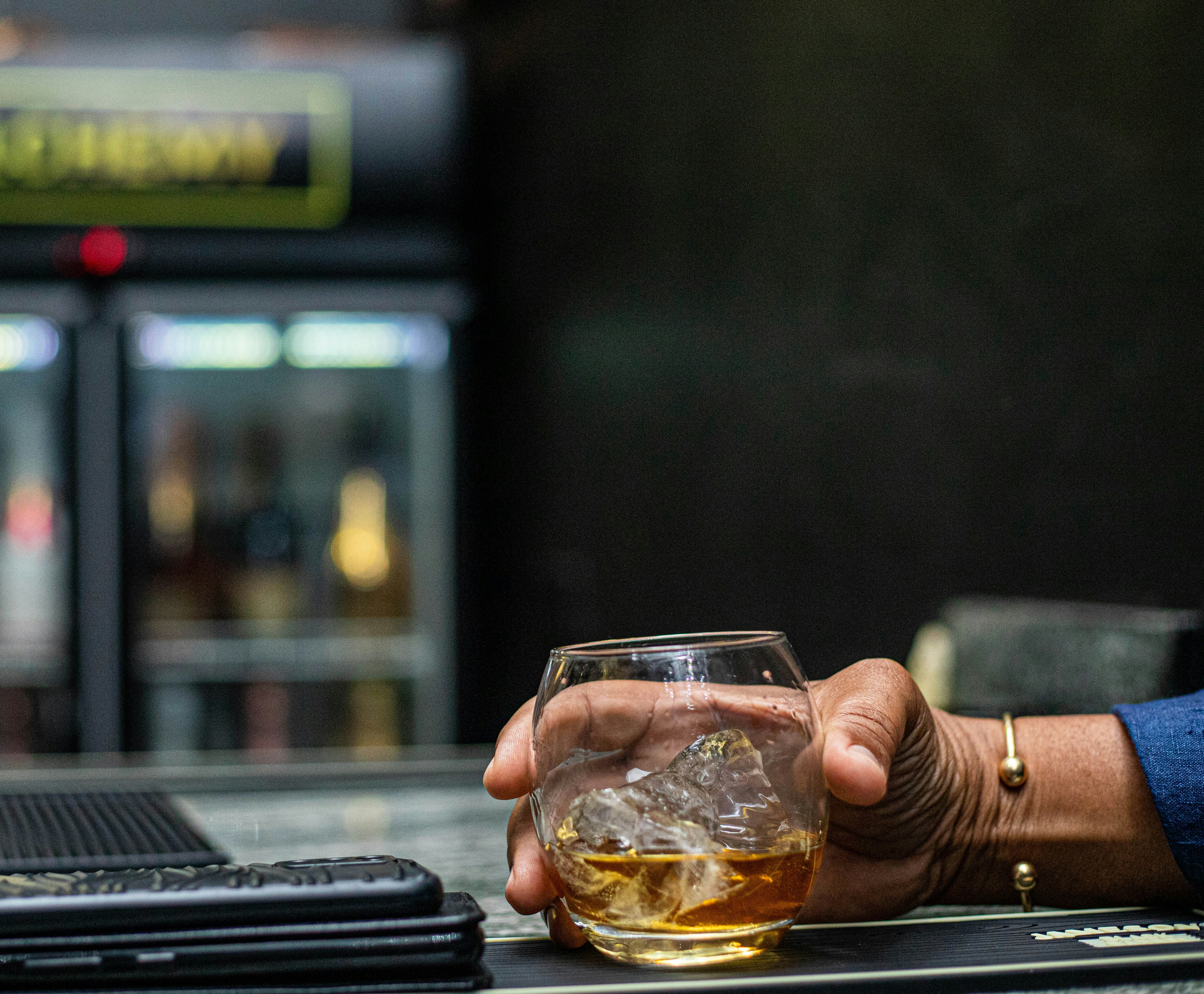 Person holding whisky on ice at a bar
