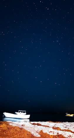 A peaceful night scene showing stars reflected on the water around the anchored boat.