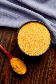 a bowl of mustard next to a spoon on a wooden table
