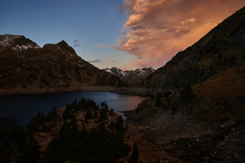a lake surrounded by mountains under a cloudy sky