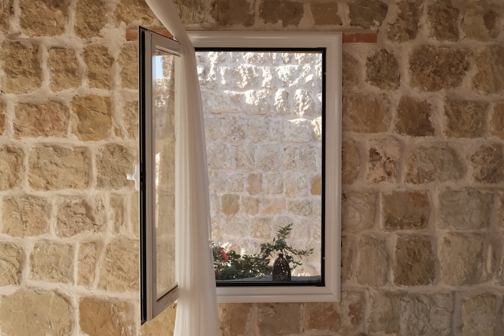 a window in a stone wall with a white curtain