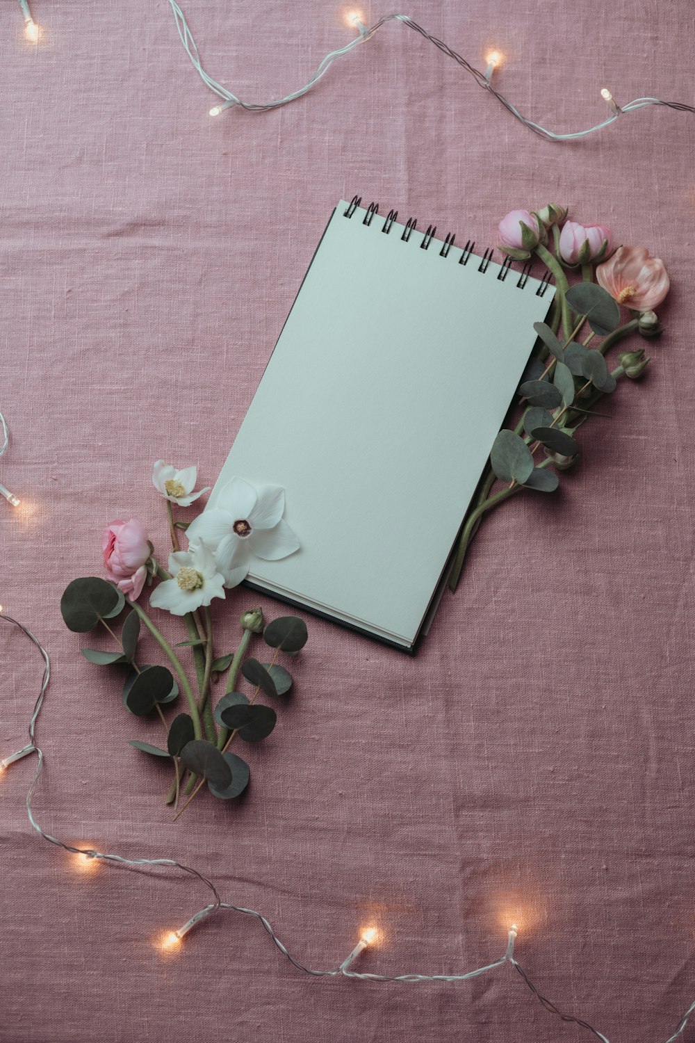 a notepad with a pen and flowers on a pink background