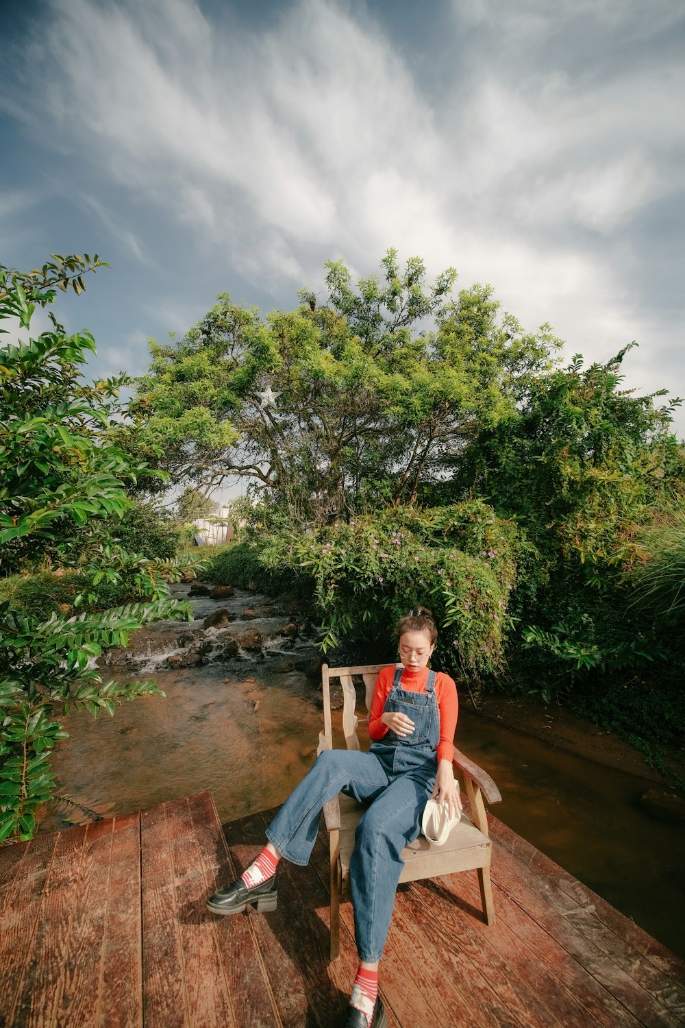 a woman sitting on a wooden bench next to a river