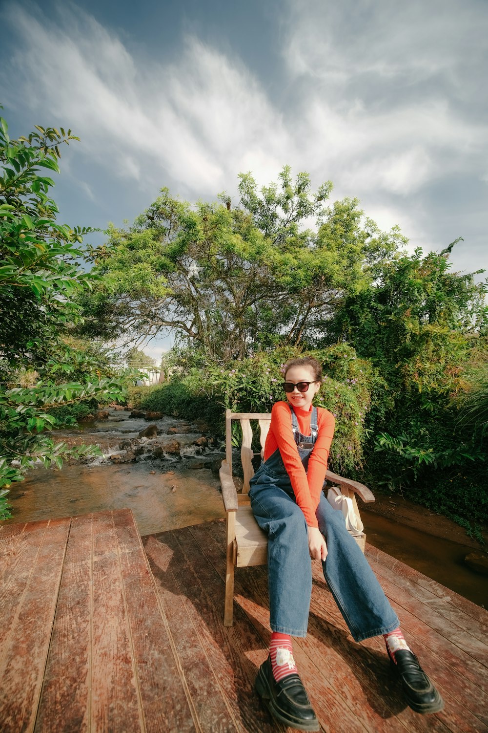 a woman sitting on a wooden bench next to a river