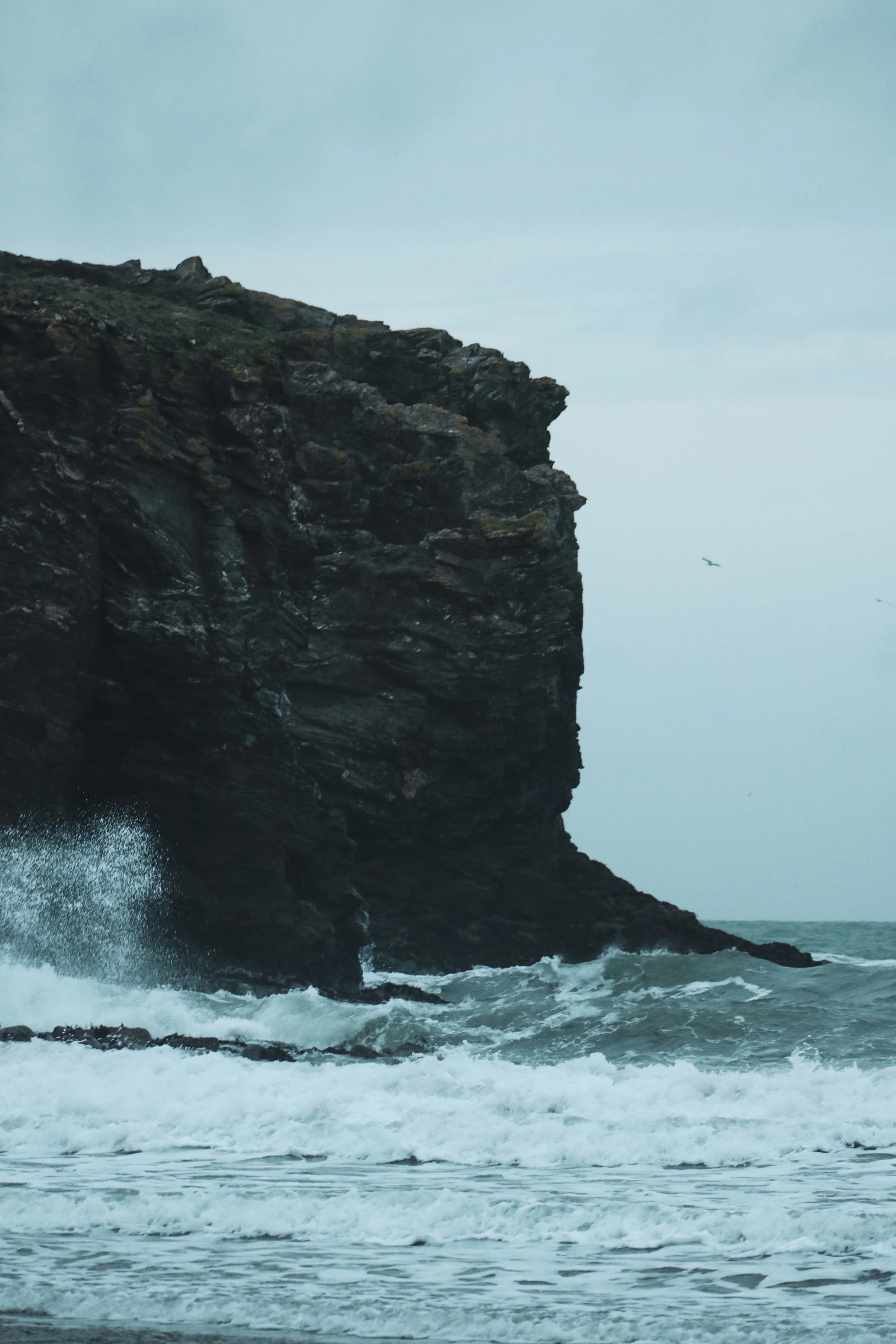 A dramatic shot of crashing ocean waves against rugged cliffs under a moody sky, capturing nature's raw power.