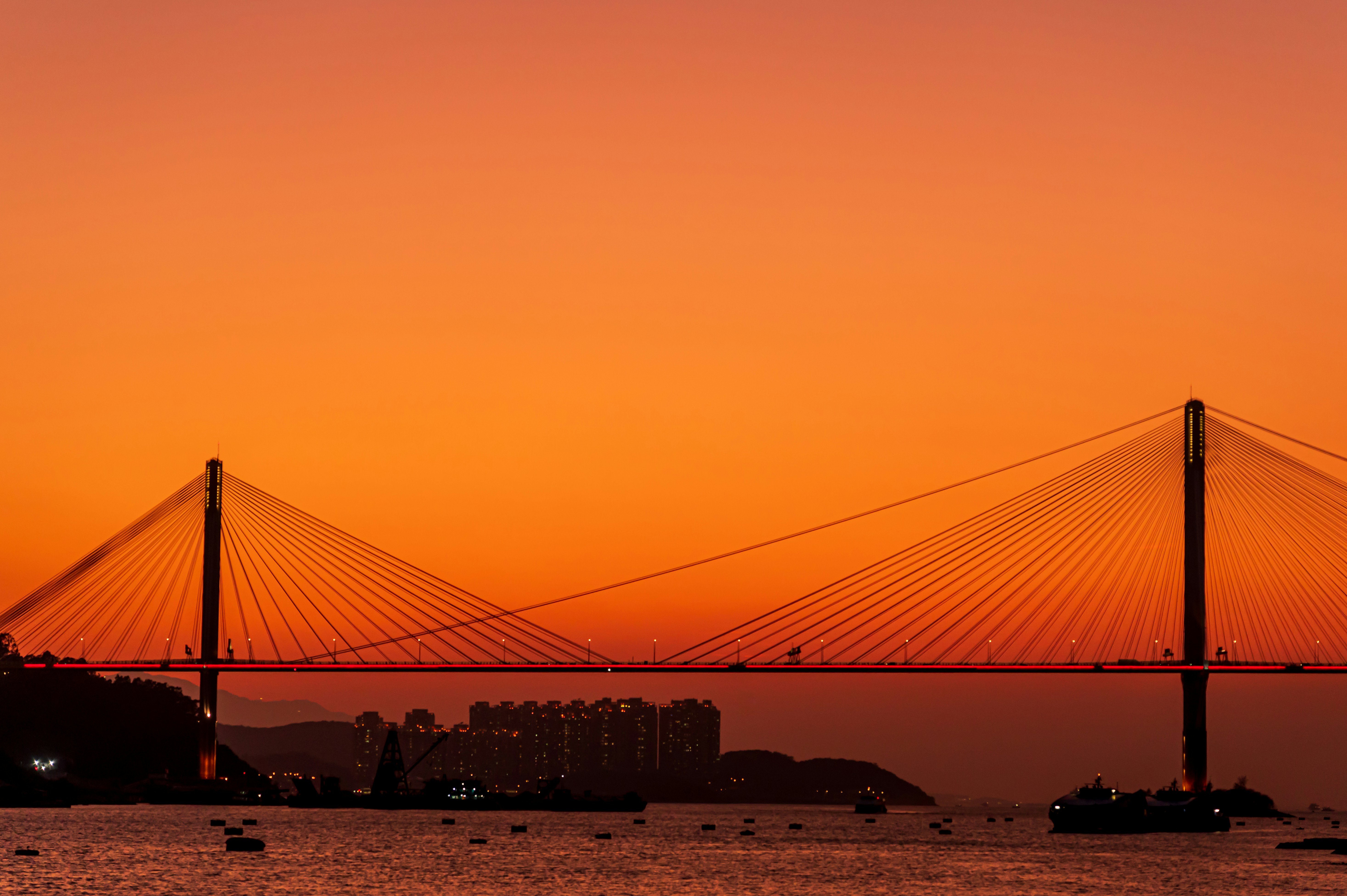 Modern cable-stayed bridge over river at sunset, dramatic orange sky, structural steel