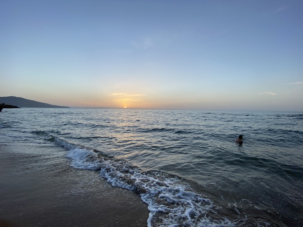 a person swimming in the ocean at sunset