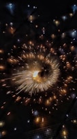 A dynamic display of golden and white sparks radiating outward against a dark backdrop, creating a dazzling effect reminiscent of fireworks or a light show.