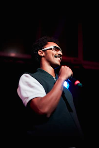 Comedian Rodolfo 'Alacrán' Samsó performing on stage with a microphone in hand.