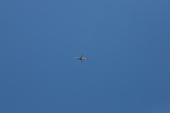 A small airplane flies across a clear blue sky, centered in the image, creating a sense of open space and vastness.