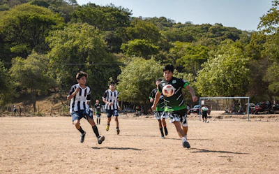 A group of young soccer players celebrating a goal on a dusty field