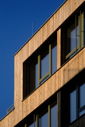 A craftsman carefully fitting wooden panels on a building facade under a clear sky.