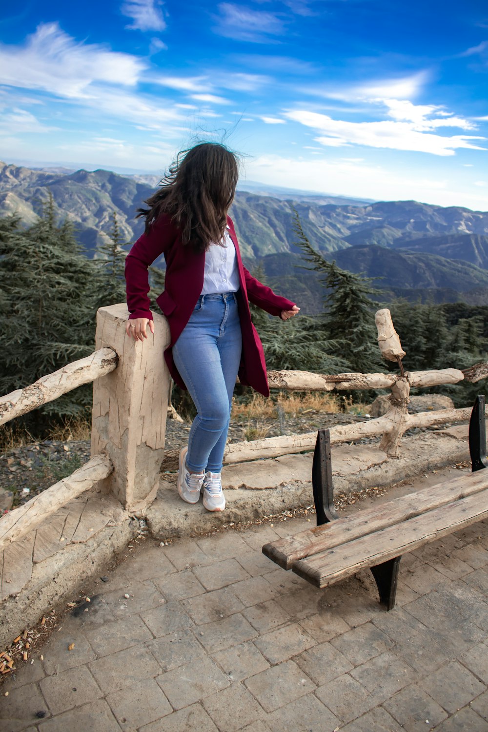a woman leaning on a wooden bench with mountains in the background