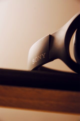 A close-up view of a Sony headphone resting on a surface with a blurred background. The focus is on the brand logo, which is clear and prominent.