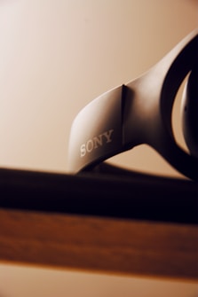 A close-up view of a Sony headphone resting on a surface with a blurred background. The focus is on the brand logo, which is clear and prominent.