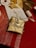 A beautifully wrapped gift rests on a red tablecloth. The box is wrapped in gold paper and adorned with a decorative string featuring small, star-shaped cutouts and bundled with white bead-like ornaments. Nearby, other wrapping materials, including a spool of ribbon and a roll of star-printed wrapping paper, are scattered, suggesting a gift-wrapping session.