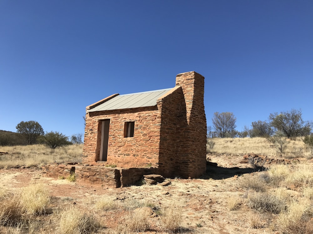 a small brick building sitting in the middle of a dry grass field
