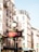 An ornate metro sign in a classic style stands prominently in front of an elegant building with cream-colored walls and traditional Parisian architecture. The building features numerous windows with decorative railings, characteristic of the city's aesthetic, under a clear blue sky.