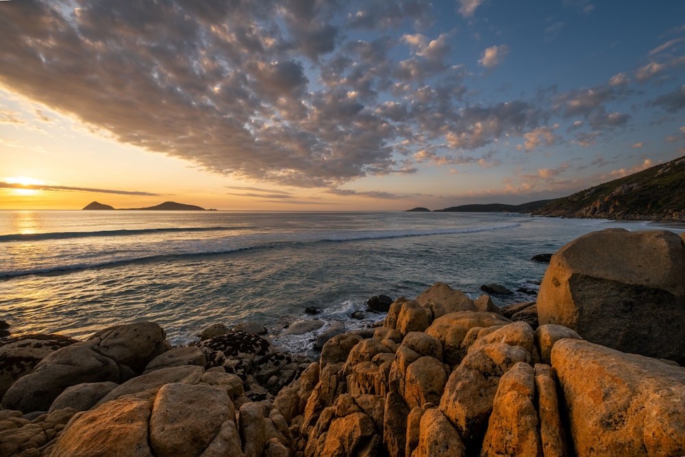 the sun is setting over the ocean and rocks