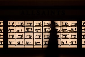 A display wall showcases a grid of vintage sewing machines, backlit to create a striking silhouette effect. In the foreground, the silhouette of a person walking by adds depth. The words 'Winter Sale Up To 40% Off' are partially visible.