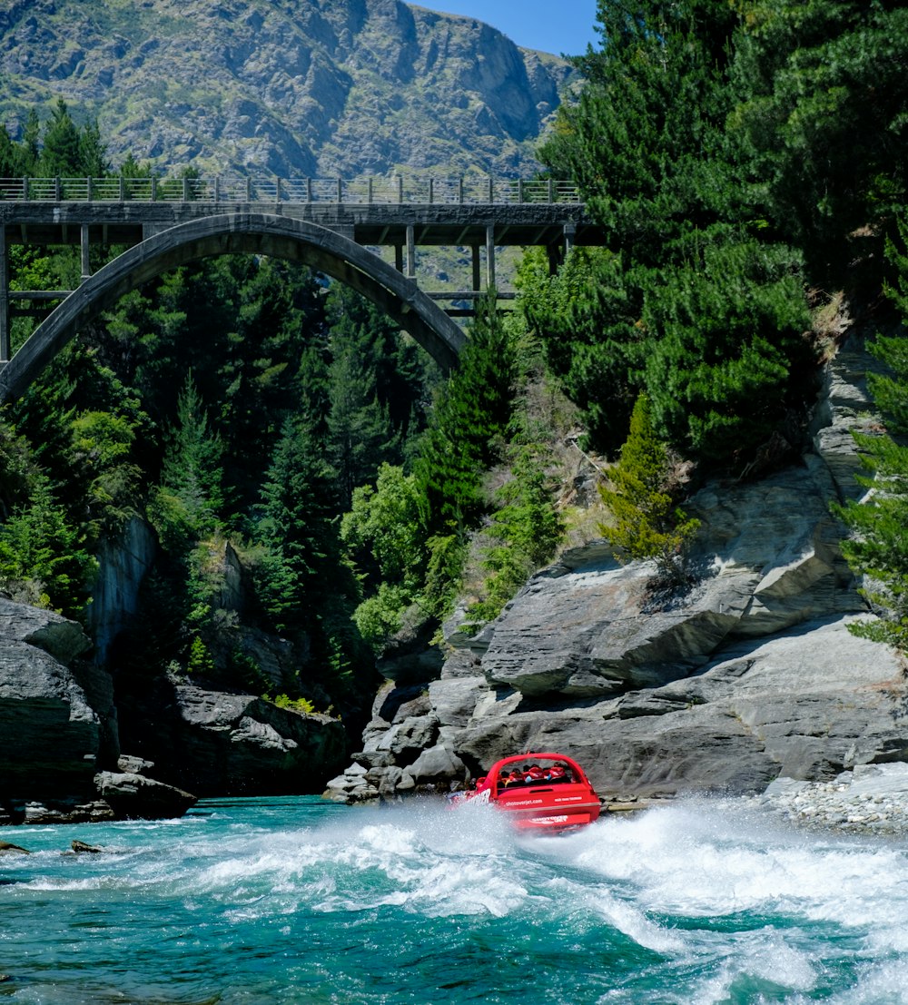 a red boat in the water near a bridge