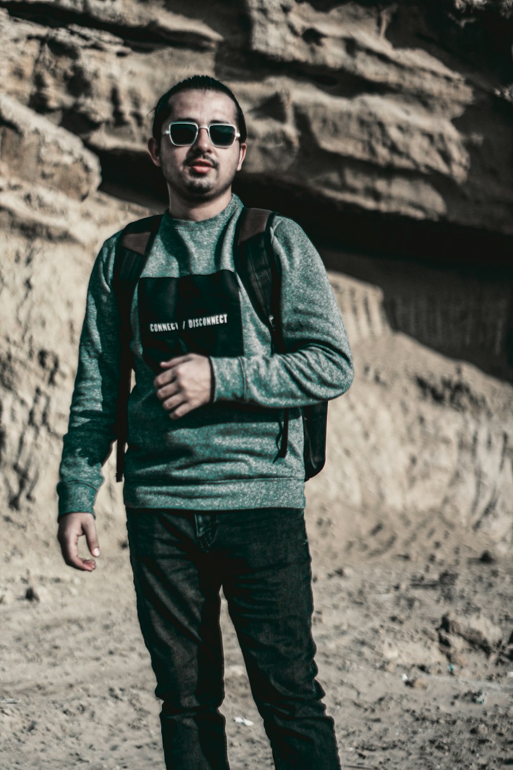 a man with a backpack and sunglasses standing in front of a mountain