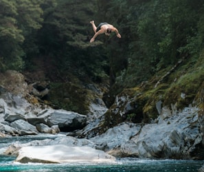 Jumping mid-air into a natural pool with towering cliffs and sun-dappled water, capturing the thrill of the tour.