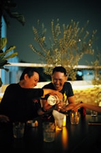 Two people laughing and chatting across a candlelit table in a relaxed cafe setting.