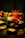 A table is set with various ingredients and cookware for a meal. There are fresh greens, sliced meats, noodles, and dumplings. A decorative dragon-head shaped pot holds cooking liquid. The dim lighting creates a warm and inviting atmosphere.