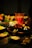 A table is set with various ingredients and cookware for a meal. There are fresh greens, sliced meats, noodles, and dumplings. A decorative dragon-head shaped pot holds cooking liquid. The dim lighting creates a warm and inviting atmosphere.