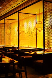 A cozy dining area features booths surrounded by ornate lattice-style wooden partitions. The warm lighting creates an inviting and intimate atmosphere. The setup includes neatly arranged tables with place settings, enhancing the elegance of the space.