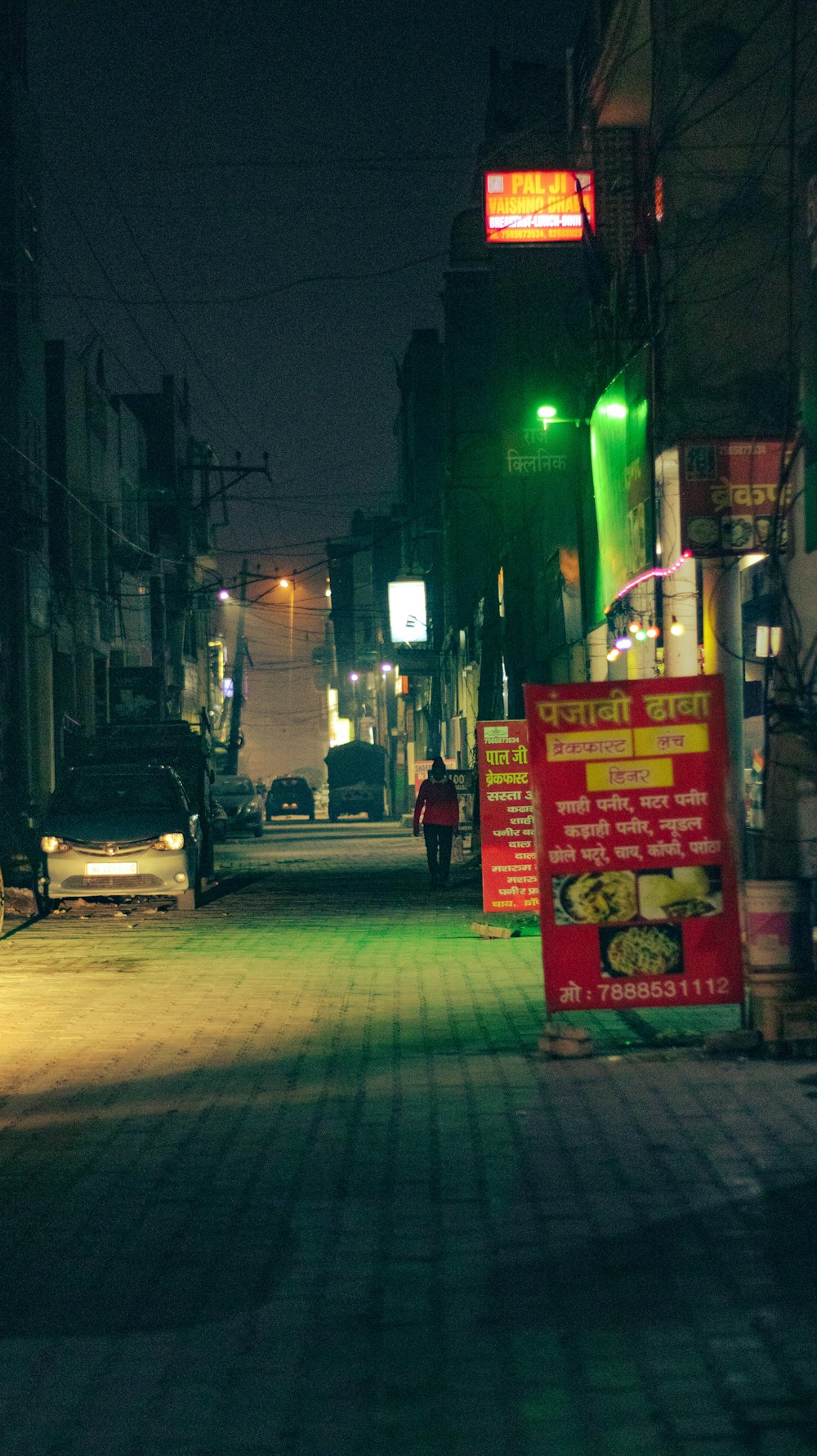 a city street at night with a person walking on the sidewalk