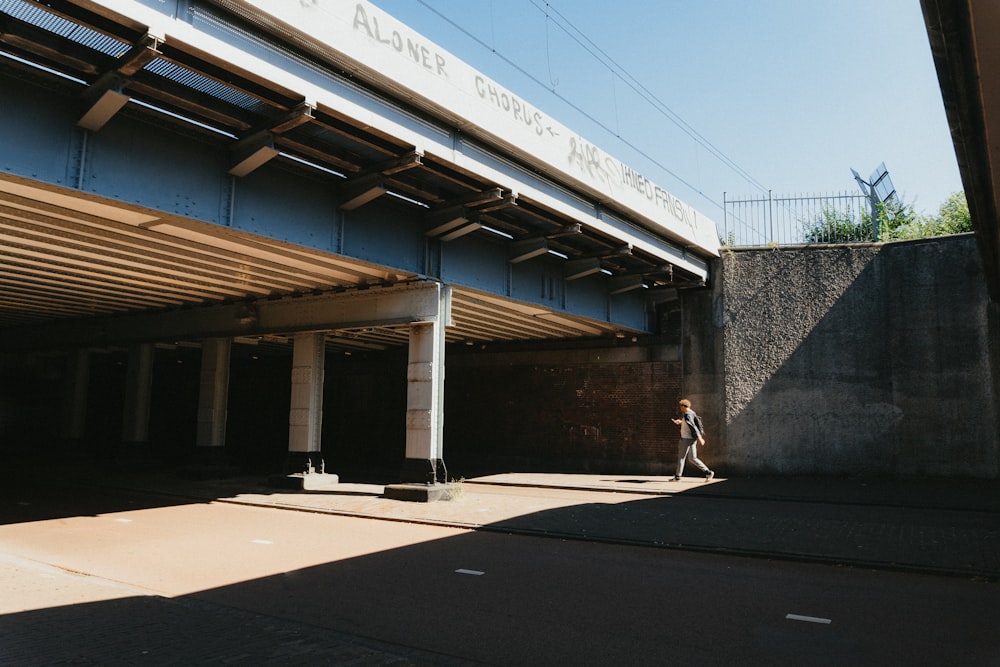 a person walking down a sidewalk under a bridge