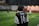A person wearing a black and white soccer jersey with the name 'Putra' and the number '14' on the back is standing on a soccer field. The field is made of artificial turf and is illuminated by lights. Additional players are blurred in the background, suggesting an ongoing soccer match or practice.