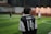 A person wearing a black and white soccer jersey with the name 'Putra' and the number '14' on the back is standing on a soccer field. The field is made of artificial turf and is illuminated by lights. Additional players are blurred in the background, suggesting an ongoing soccer match or practice.