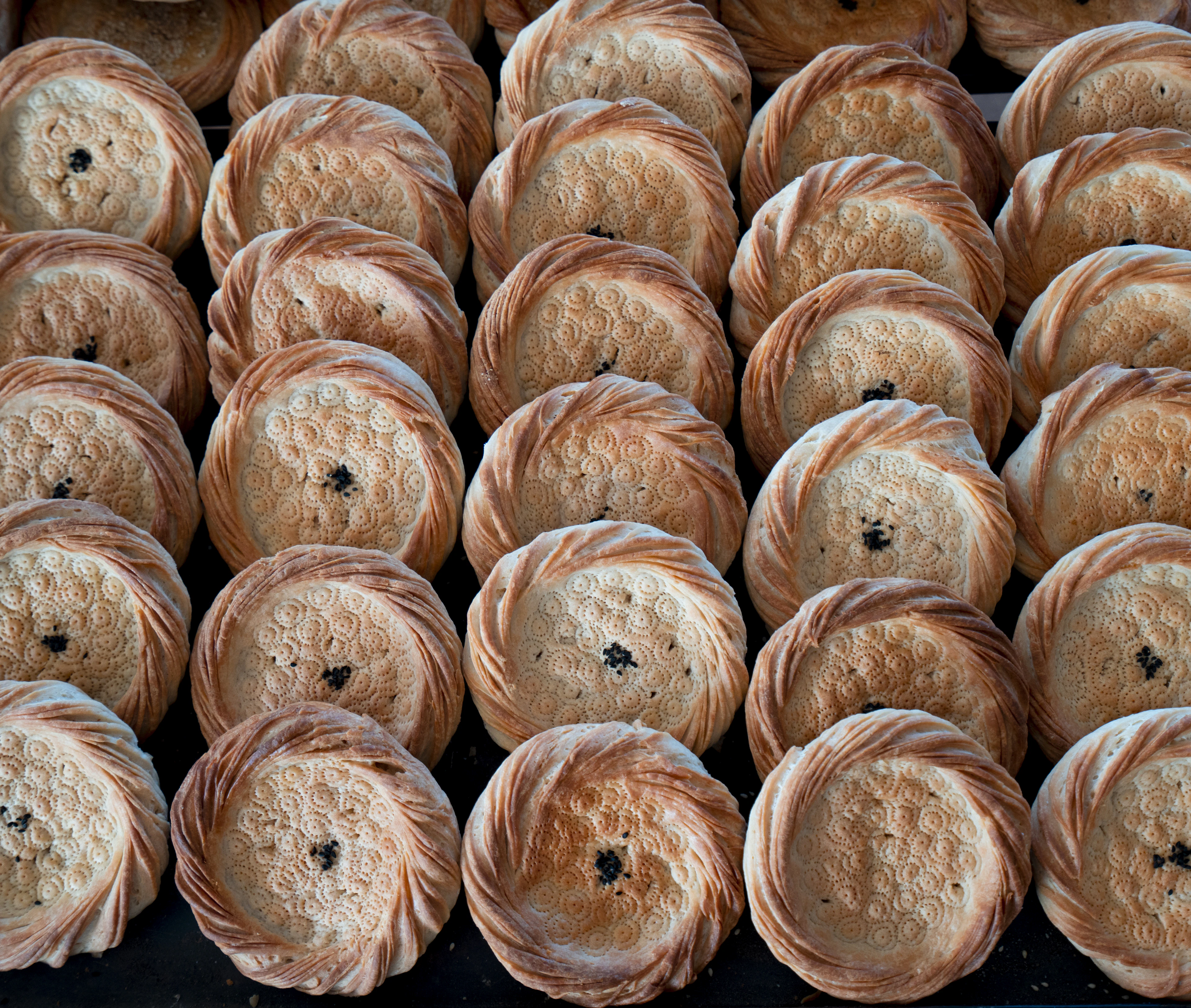 Rows of freshly baked round non flatbreads with stamped centers stacked at an Uzbek bakery stall