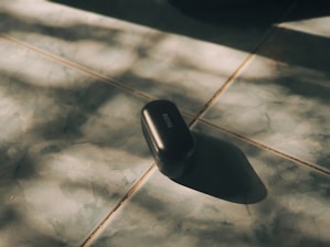 A sleek black phone case with reinforced corners lying on a wooden desk beside a charging cable.