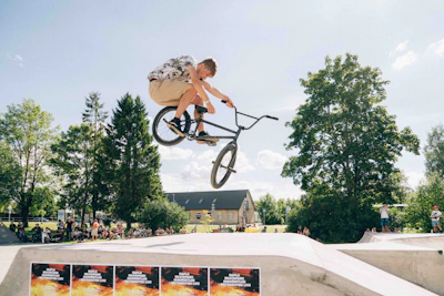 A vibrant group of BMX riders performing tricks together at sunset in an urban park.
