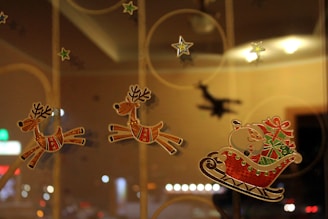 Three reindeer stickers are placed on a glass surface, appearing to pull Santa Claus in a sleigh laden with gifts. Star stickers are scattered around, adding to a festive atmosphere. The background features soft lighting and a blurred shadow of Santa, enhancing the holiday theme.