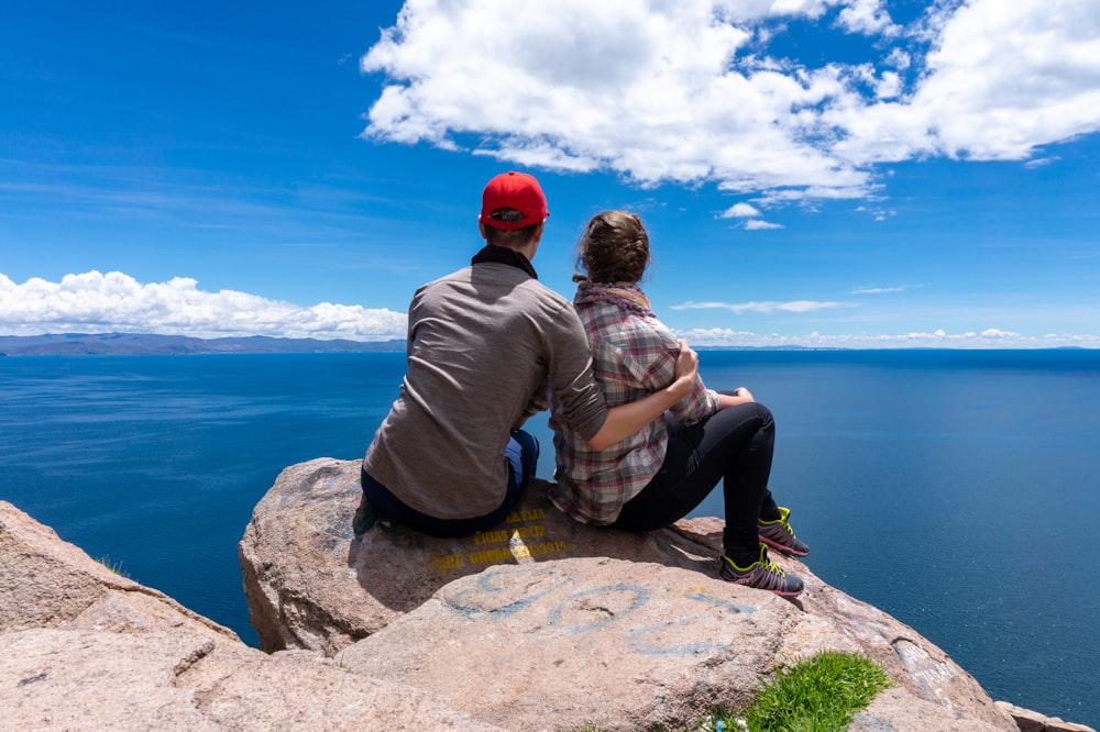 a man and a woman sitting on top of a large rock