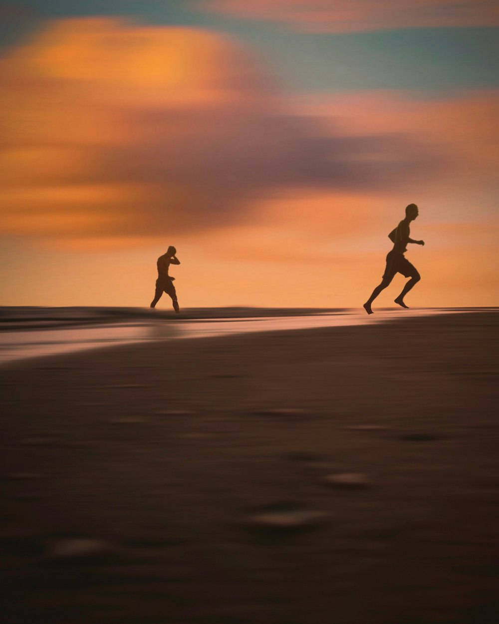 two people running on the beach at sunset